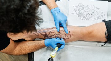 Top view of an unrecognizable tattoo artist tattooing an octopus design on his client's leg.
