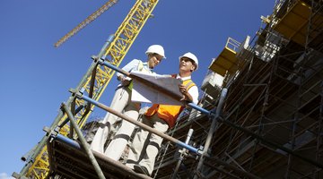 Two Well Dressed Colleagues Standing Side by Side on a Construction Frame, Looking at Blueprints